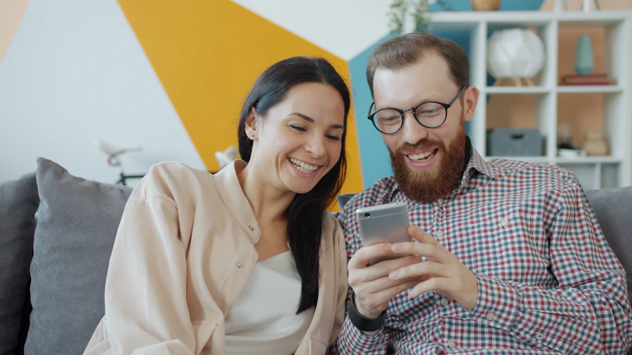 A couple smiling at a phone on their sofa